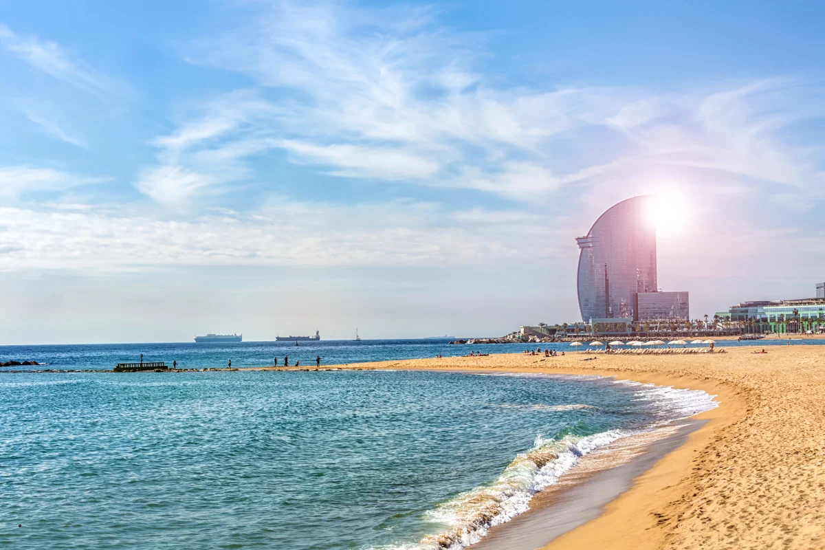 Sorra i mar en calma amb la silueta de l'Hotel Vela al fons de la platja
