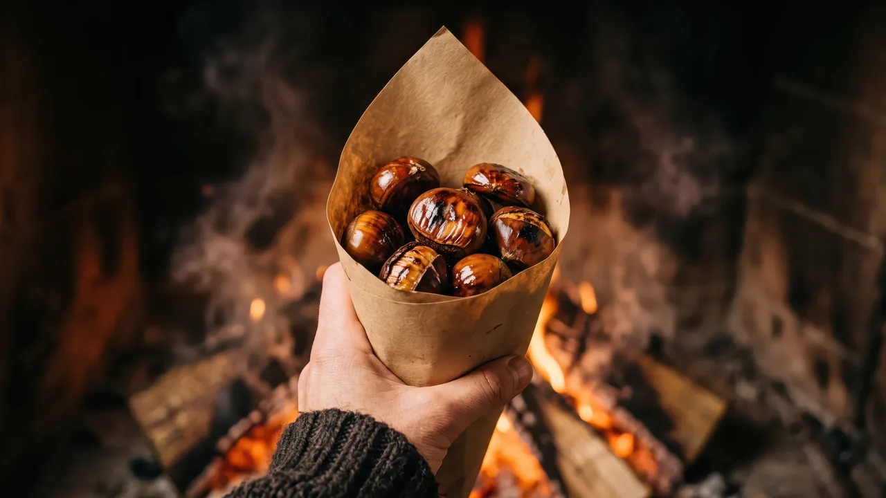 Mano sosteniendo una paperina de castañas asadas delante de un fuego de leña, la imagen de la Castanyada en Barcelona