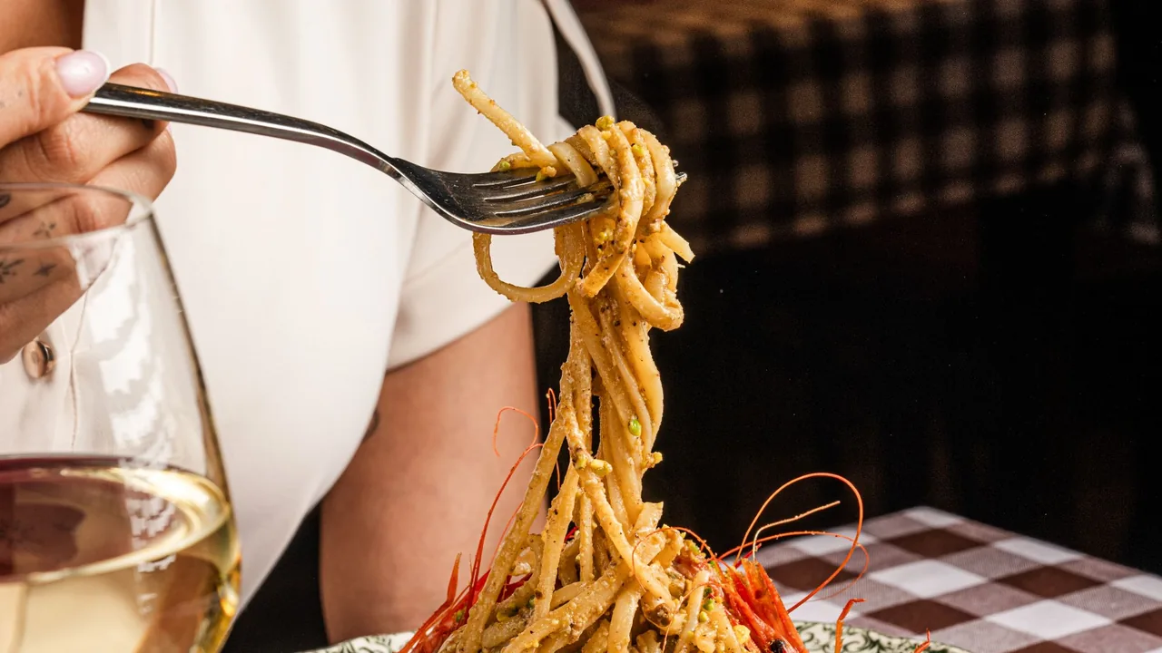 Comensal enrollando espaguetis con langostinos en un tenedor junto a una copa de vino blanco en un restaurante de Barcelona