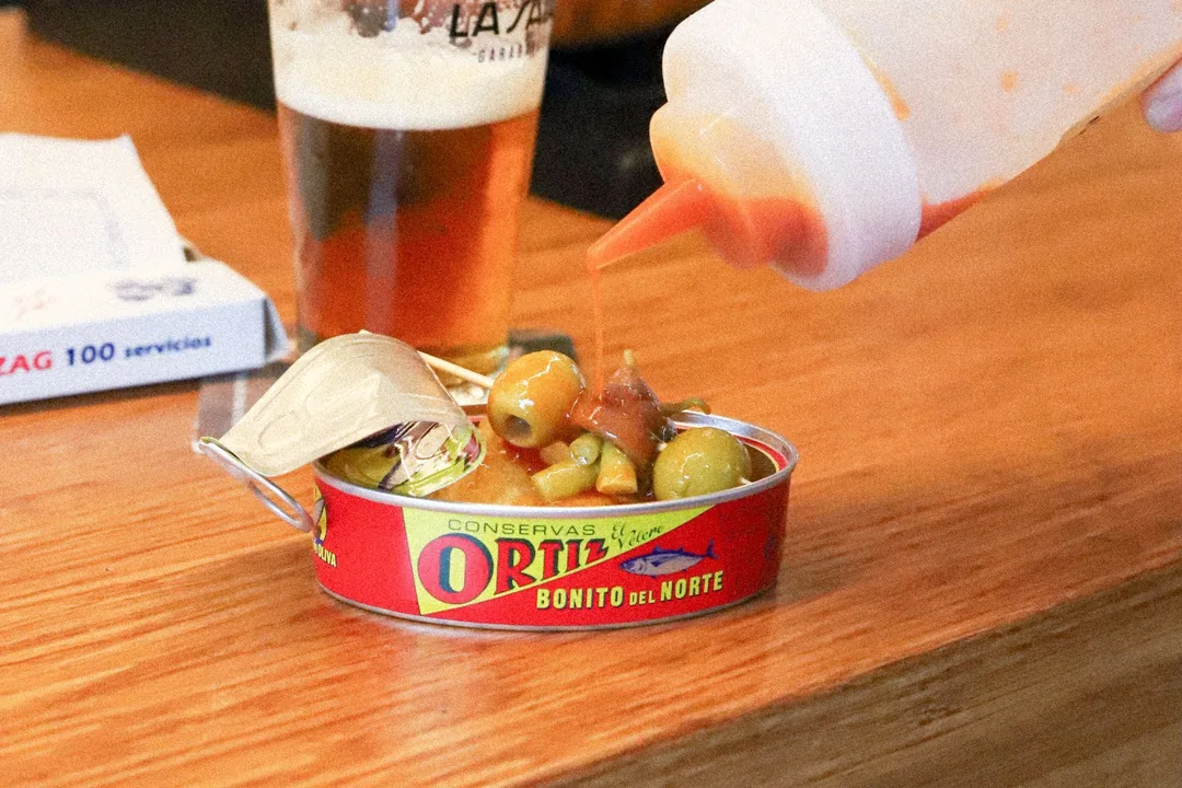 Caña de cerveza y lata de conservas con aceitunas en una barra de madera