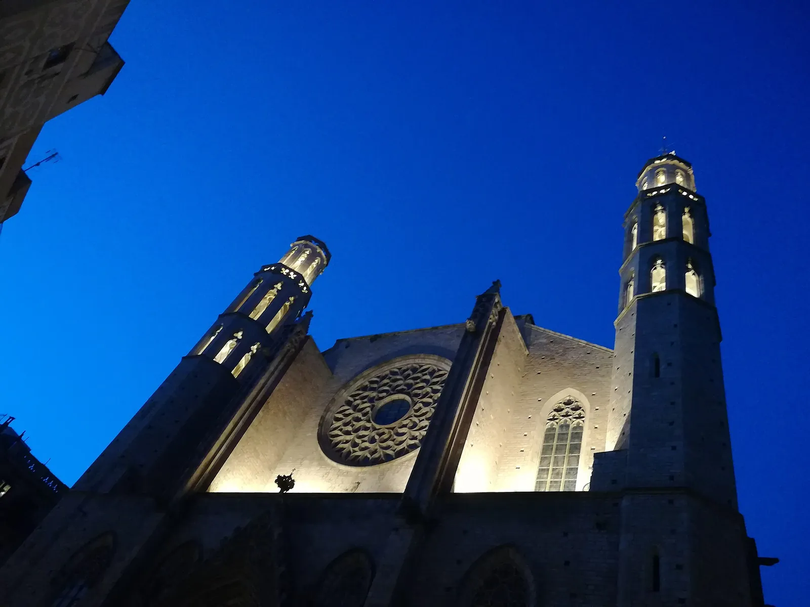 Fachada de la basílica de Santa Maria del Mar iluminada de noche, con el rosetón y los dos campanarios